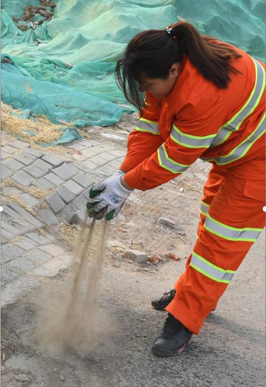图为李萌用沙土掩盖抽粪车作业时洒漏在街边的粪水，以减少气味
